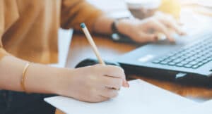 closeup-of-persons-hands-writing-while-using-laptop-cropped