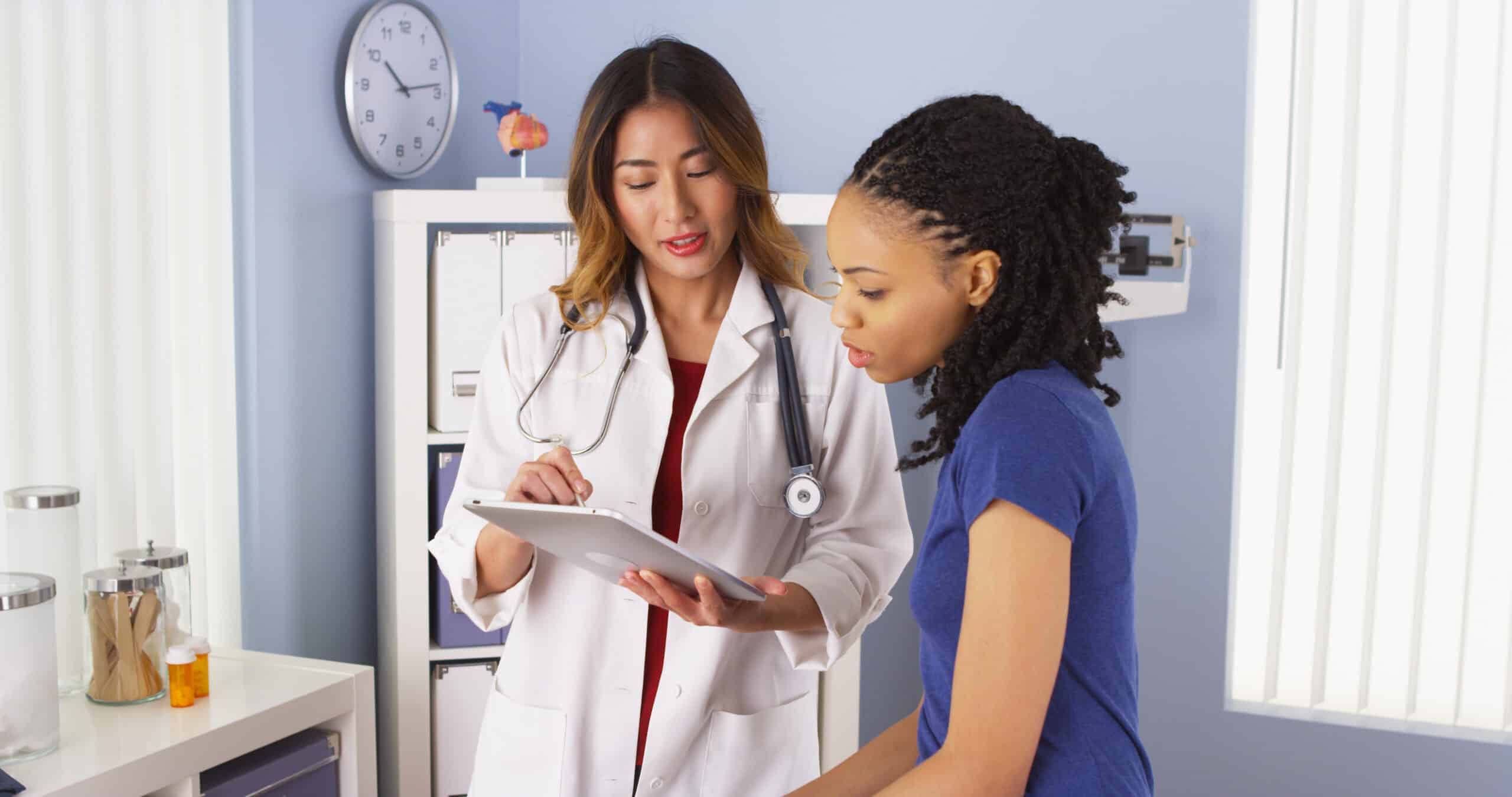 African American patient explaining issues to Asian doctor using tablet Woman discussing blood clot risk factors with doctor