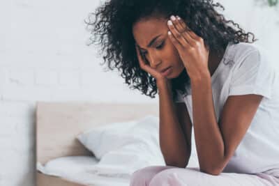 pretty african american woman holding hands near head while suffering from headache in bedroom CVST is a rare form of stroke.
